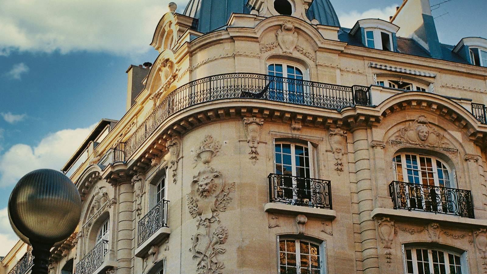 Angle arrondi d’un immeuble parisien, surmonté d’un dôme vert-de-gris, sous un ciel bleu